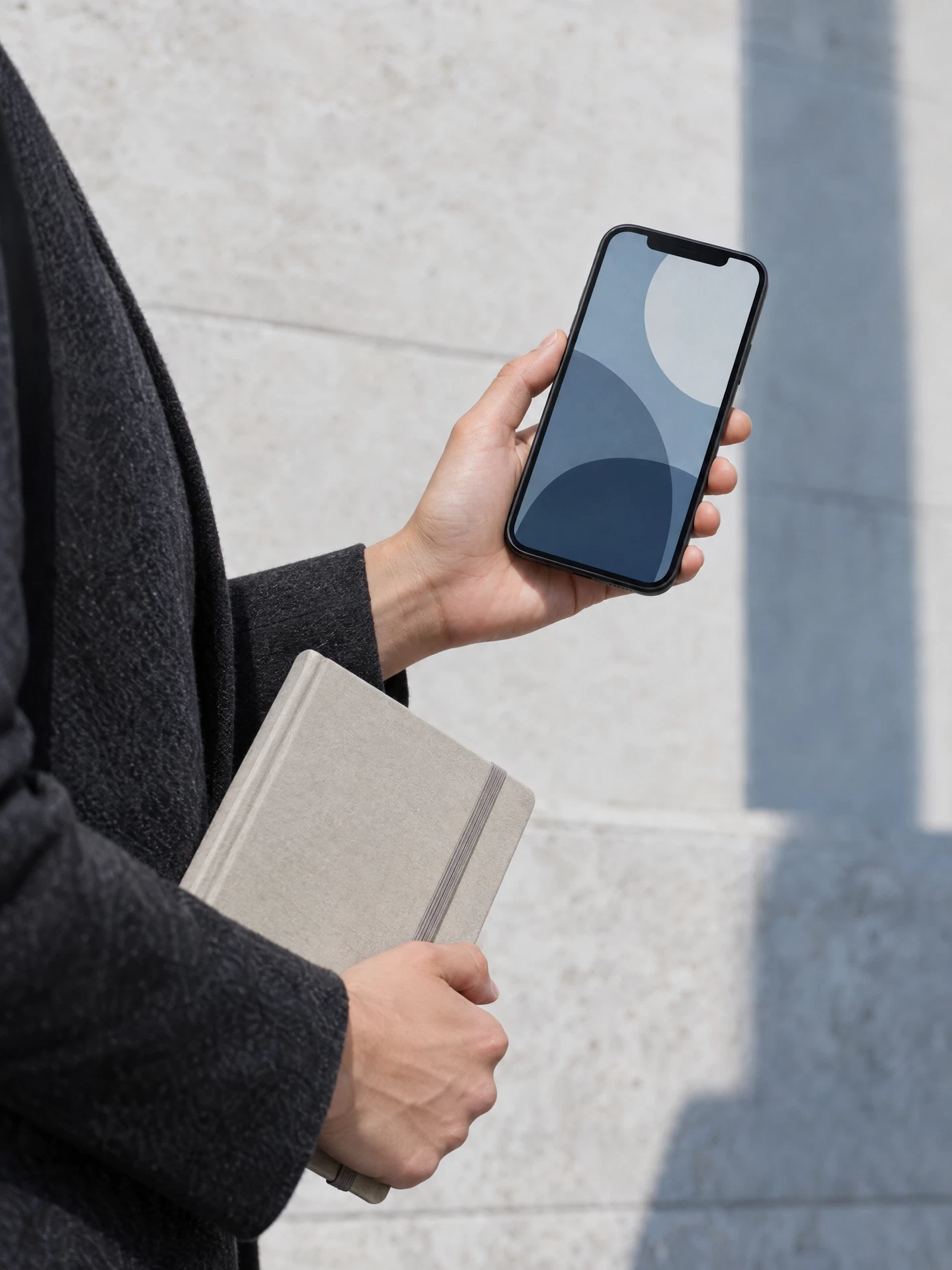 Hand holding an unbranded phone and closed notebook in a neutral setting
