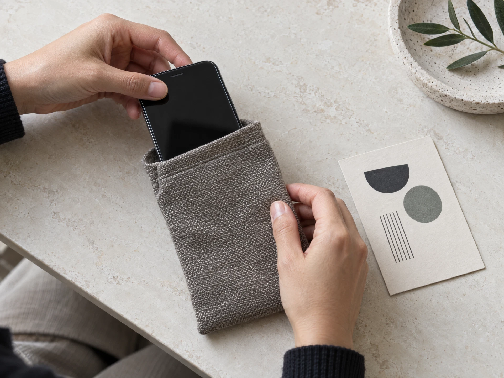 Hands placing a generic phone into a fabric pouch beside an abstract card